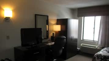 A hotel room with a desk, chair, television, wardrobe, and a window with curtains.