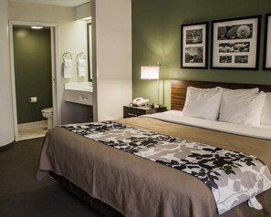 A hotel room with a bed, a bedside table with a lamp, a mirror, and a framed picture on the wall.