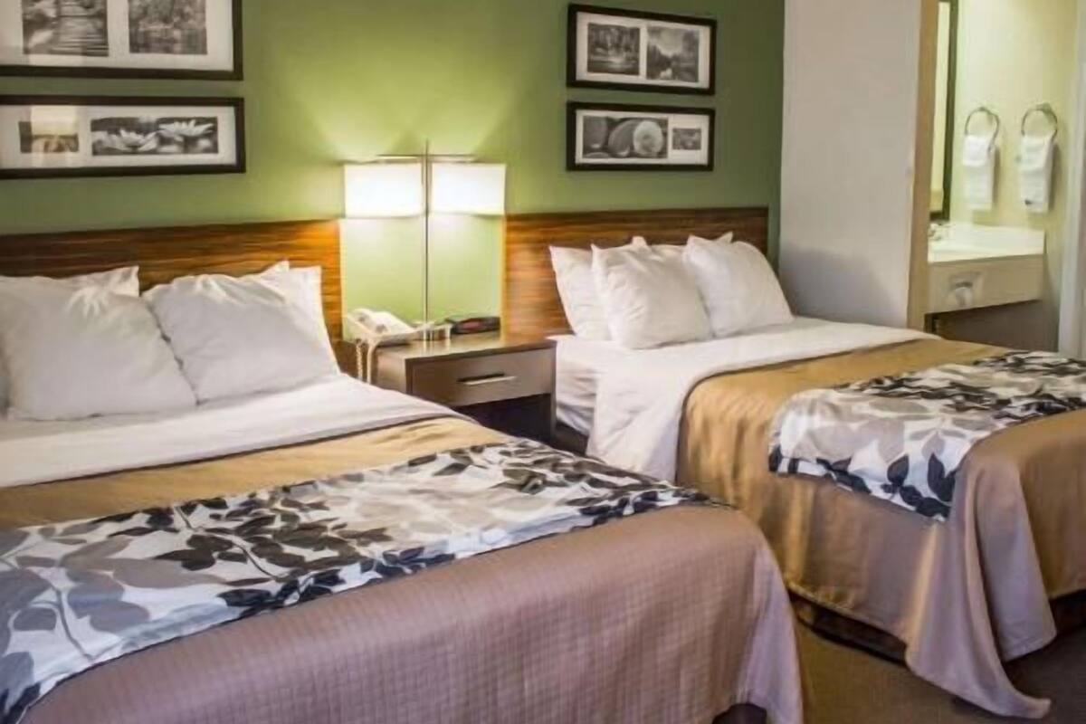 Ein Hotelzimmer mit zwei Betten, einem Nachttisch, einer Lampe und gerahmten Bildern an der Wand.