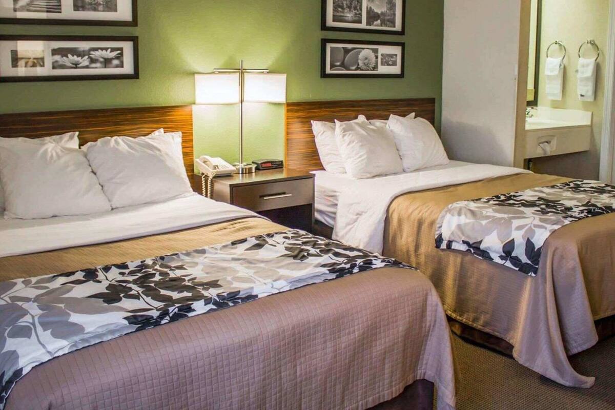 Ein Hotelzimmer mit zwei Betten, einem Nachttisch, einer Lampe und gerahmten Bildern an der Wand.