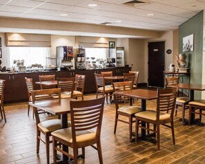 A restaurant with wooden tables and chairs, a kitchen area, and a green wall with a picture.