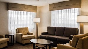 A hotel room with a sofa, armchairs, a coffee table, and a lamp. - Suburban Studios Johnstown - Richland Town Center (Johnstown)