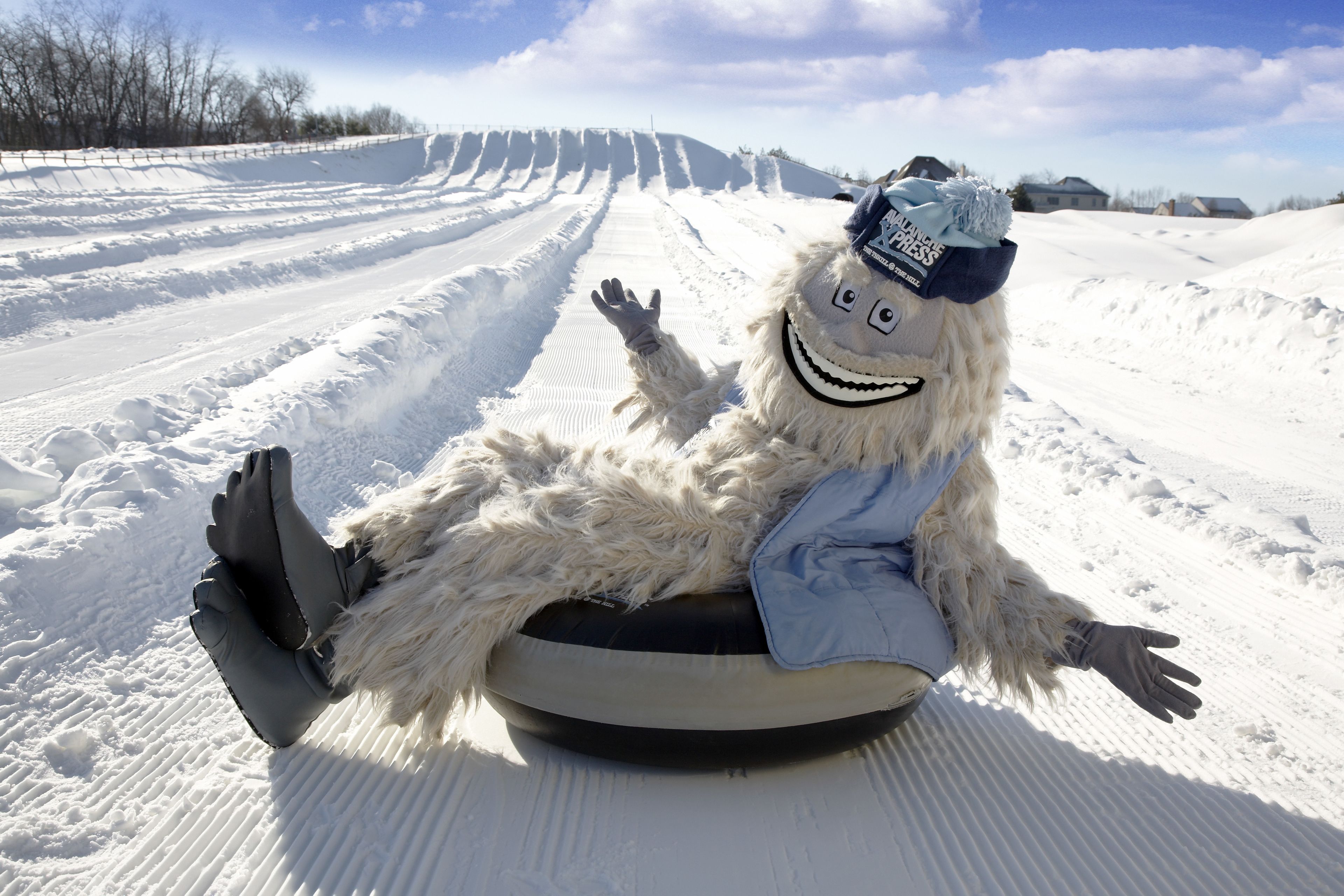 Eine Person in einem flauschigen Kostüm sitzt auf einem Schlitten in einem verschneiten Hang.