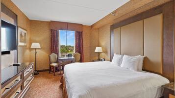 A hotel room with a large bed, a desk with a chair, a TV, and a window with curtains.