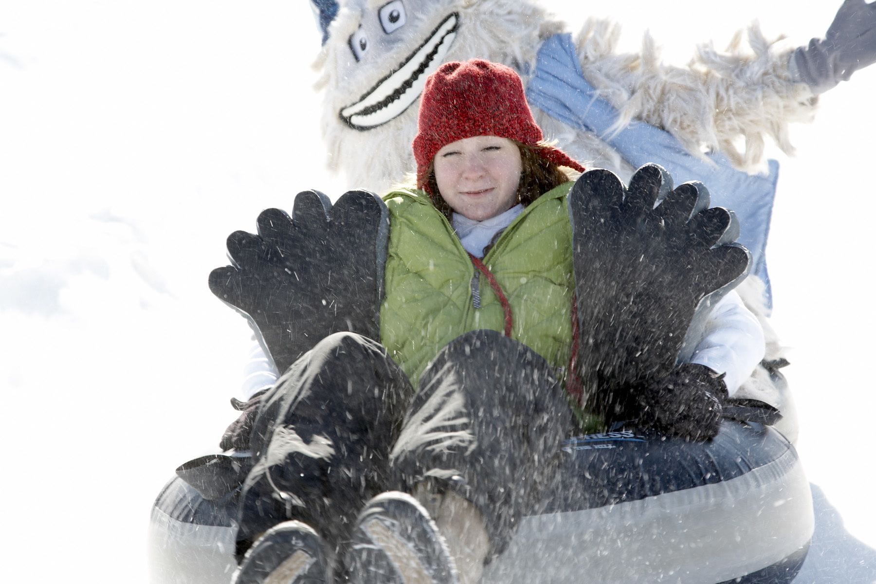 A person in a green jacket and red hat riding a snow tube.