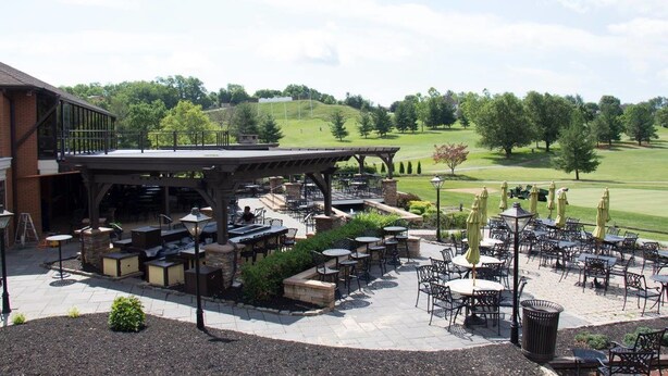 An outdoor patio area with multiple tables and chairs, a covered seating area, and a view of a golf course in the background. - Heritage Hills Golf Resort (York)