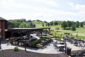An outdoor patio area with multiple tables and chairs, a covered seating area, and a view of a golf course in the background. - Heritage Hills Golf Resort (York)