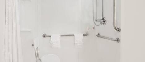 Un baño blanco con ducha, barras de apoyo y una silla blanca.