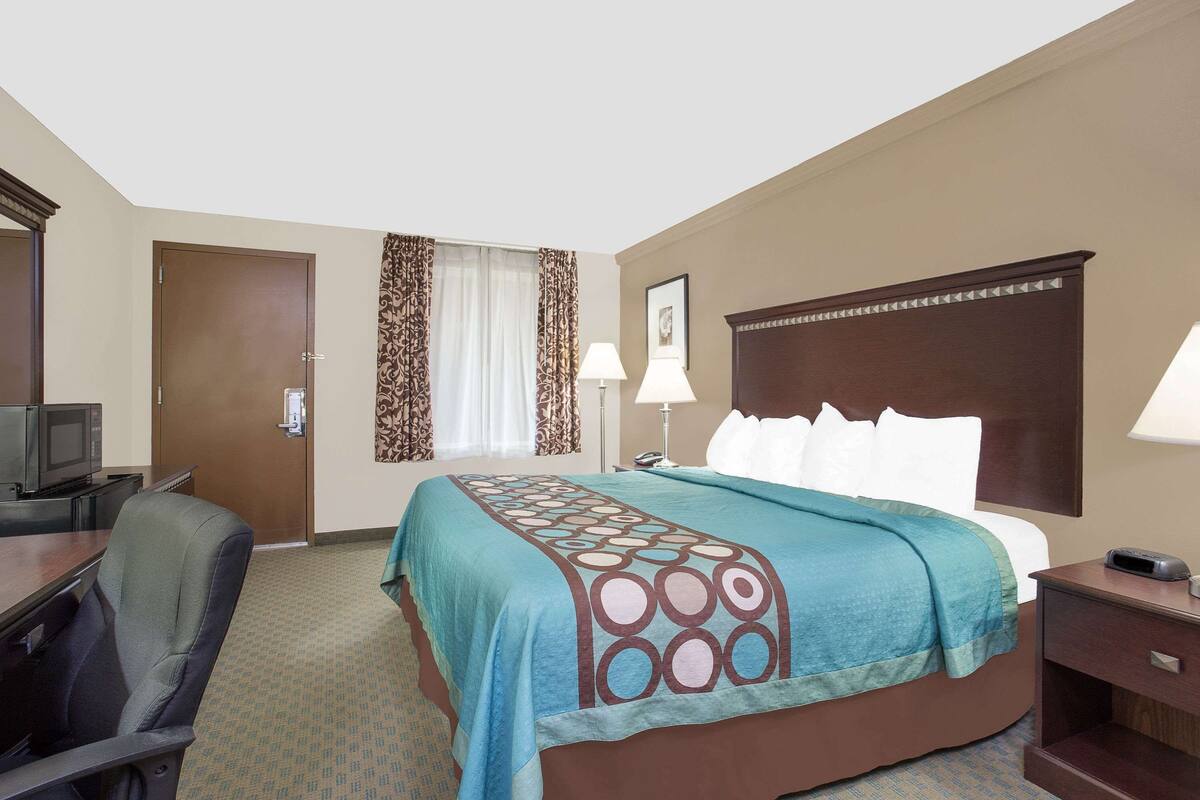 Een hotelkamer met een bed, een bureau met stoel, een televisie en een raam met gordijnen.