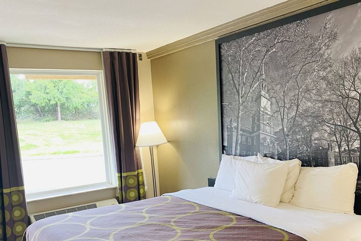 Een hotelkamer met een groot bed, een raam met gordijnen, een wandlamp en een groot schilderij.