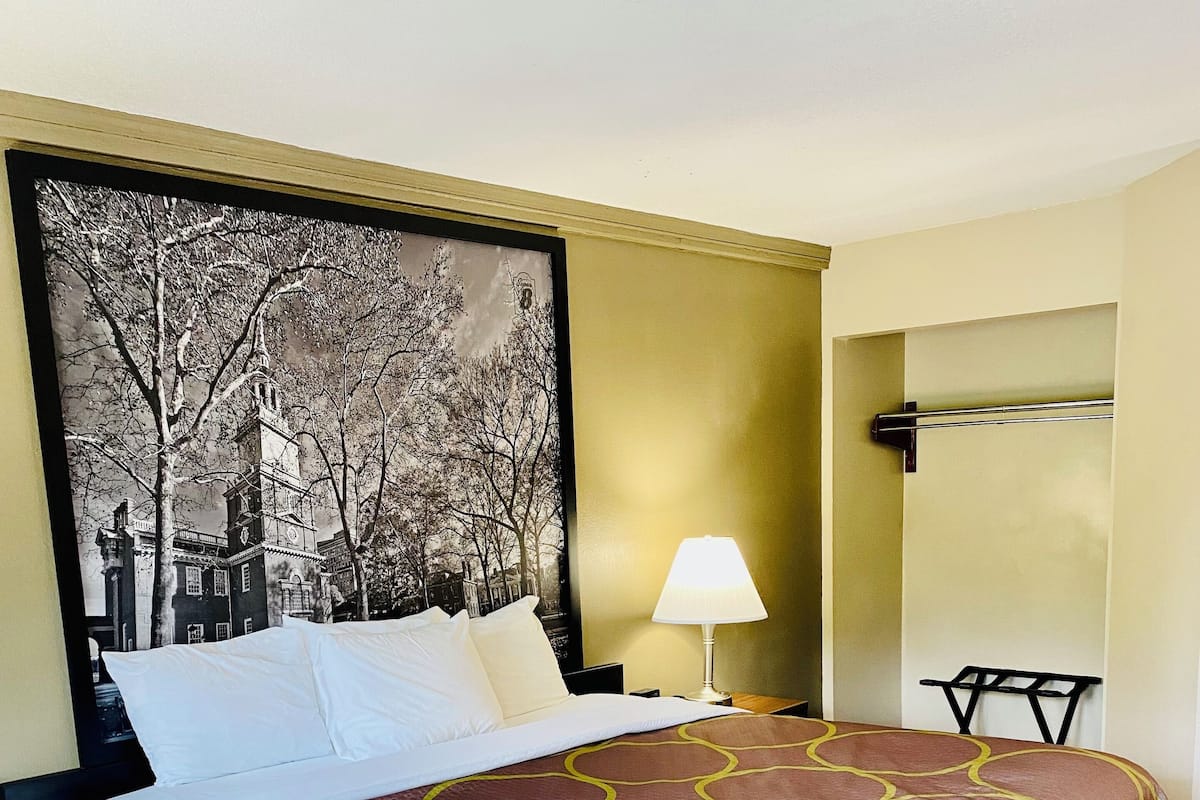 Hotelkamer met een bed, nachtkastje met lamp, een wandrek voor handdoeken en een groot gepresenteerd fotokader met een gebouw.