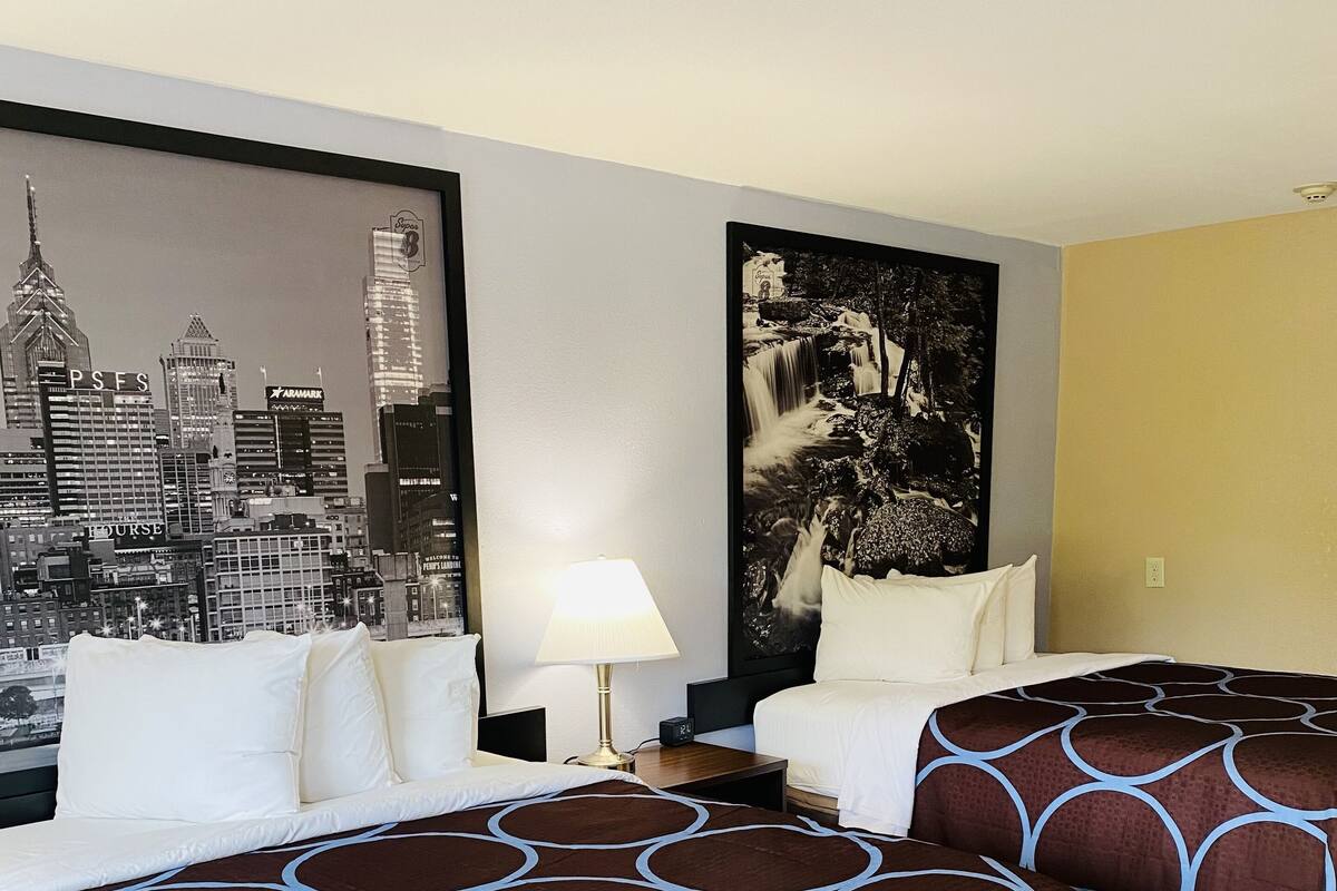 Een hotelkamer met twee bedden, een stadsgezicht muurschildering, een afbeelding van een waterval en een lamp.