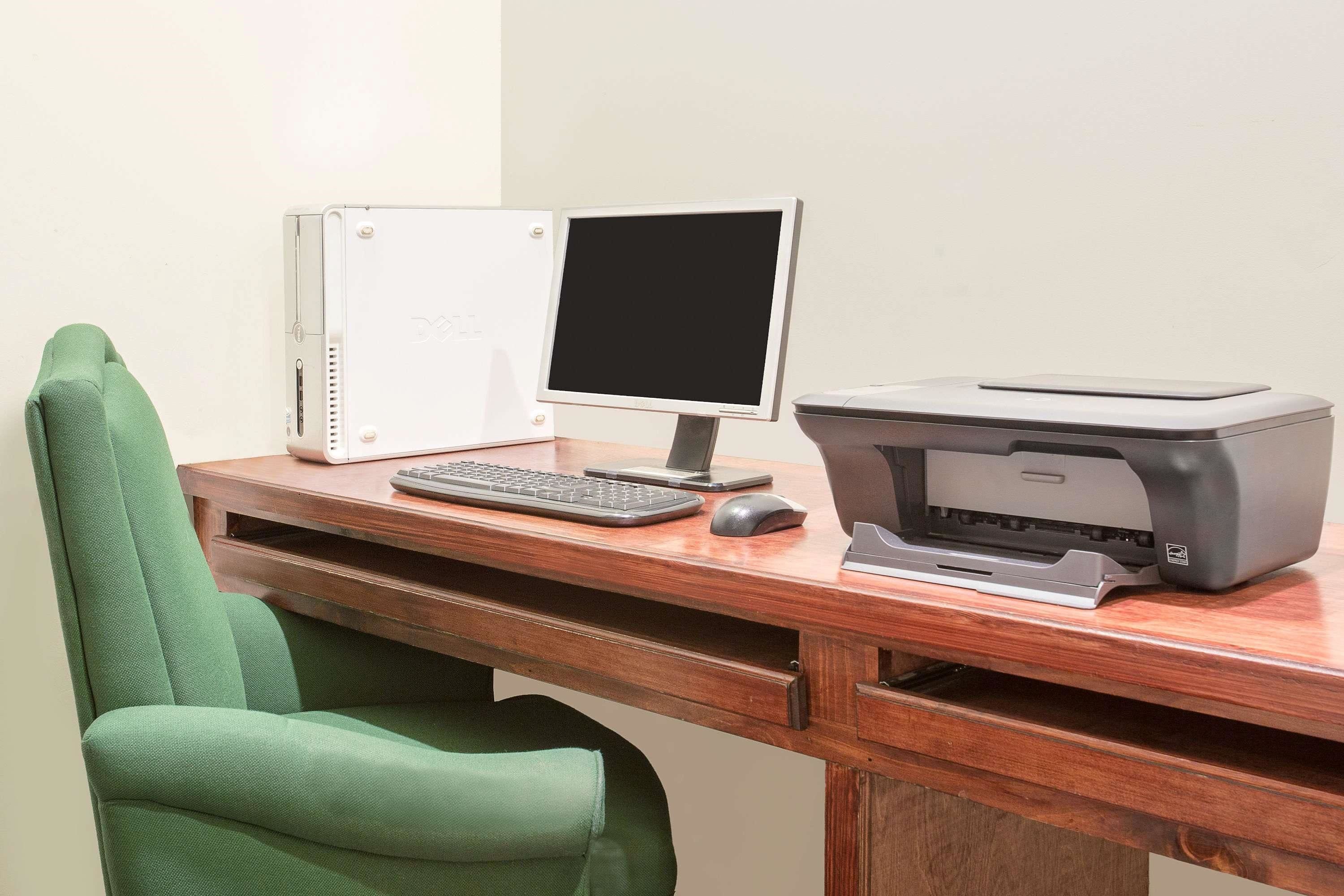 A wooden desk with a desktop computer, a printer, and a green office chair.