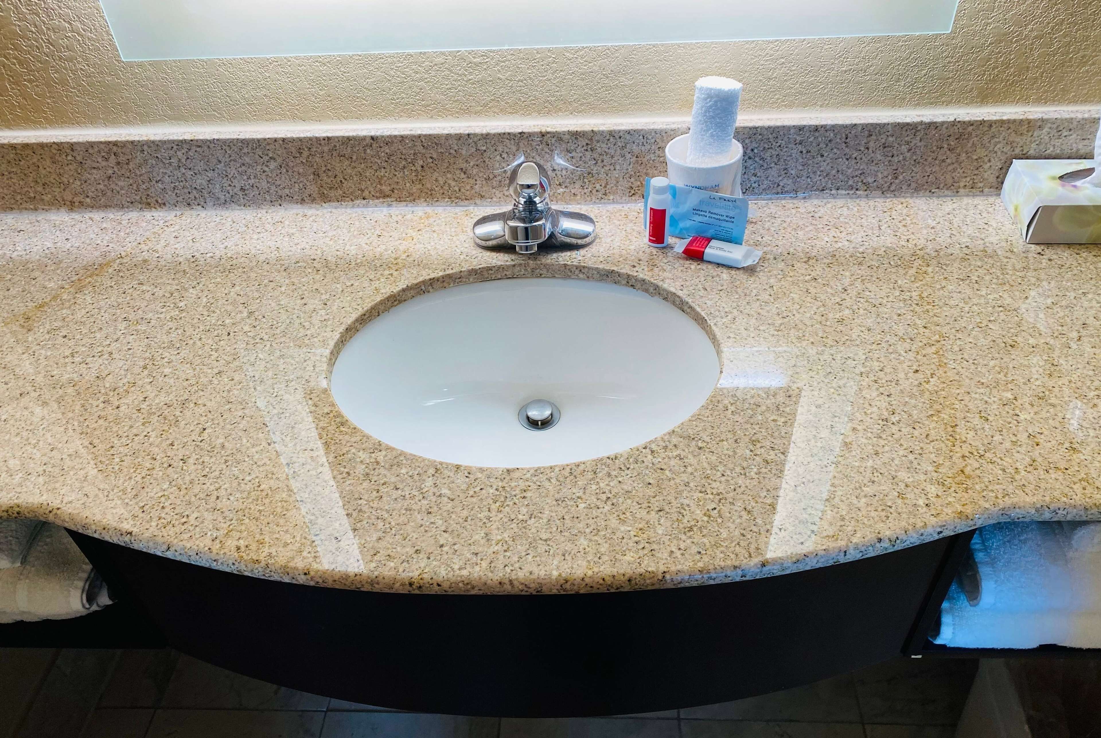 A bathroom sink with a granite countertop, a silver faucet, and toiletries including a bottle of hand soap and a tube of toothpaste.
