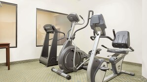 Un gimnasio con tres bicicletas estáticas, una cinta de correr y una pequeña mesa de madera.