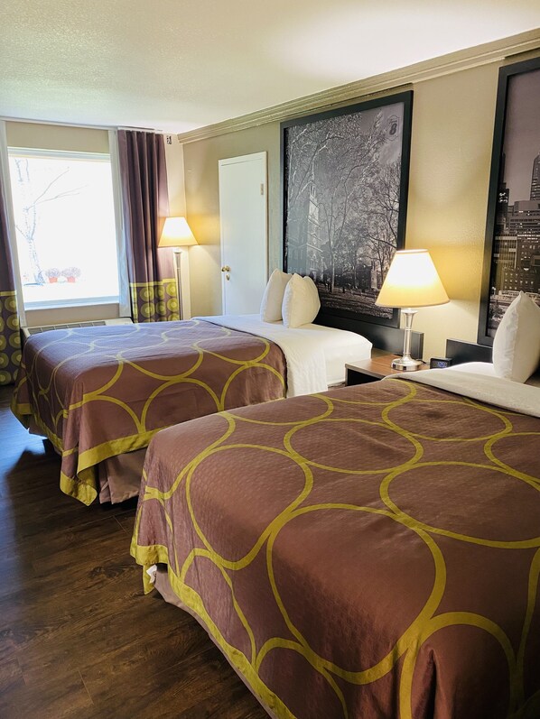 Hotelkamer met twee bedden, een groot raam met gordijnen, een aan de muur hangend schilderij en een nachtkastje met een lamp.