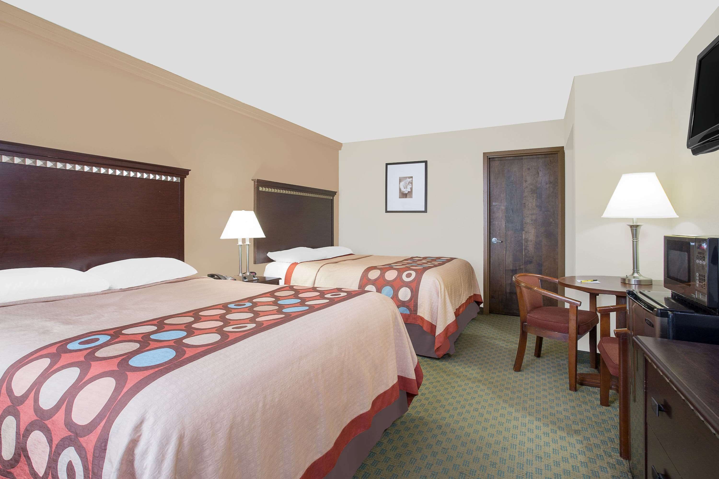 A hotel room with two beds, a desk with a chair, a television, and a door.