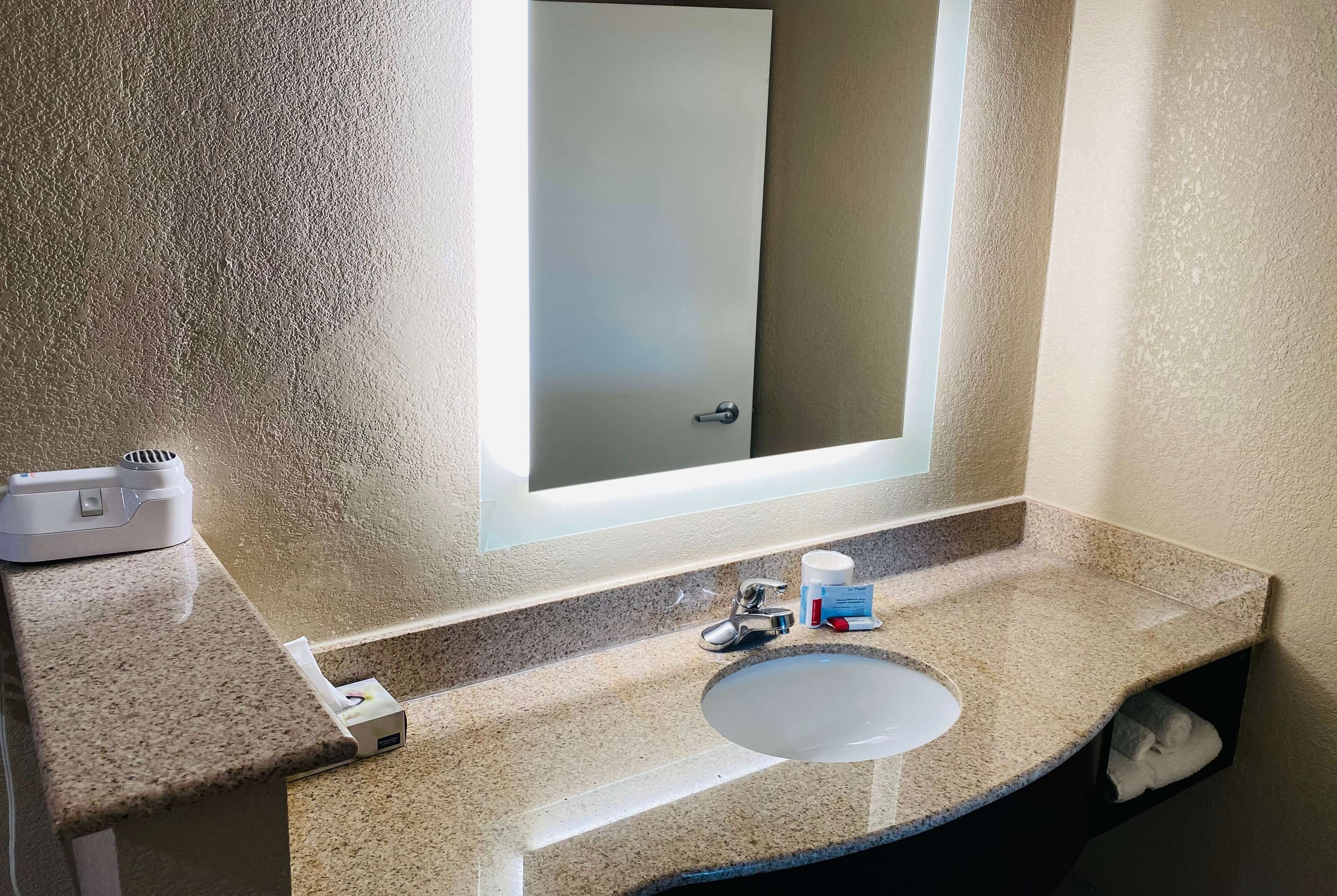 Un baño con encimera de granito, un lavamanos, un espejo y un perchero para toallas.