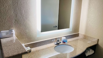 Un baño con encimera de granito, un lavamanos, un espejo y un perchero para toallas.