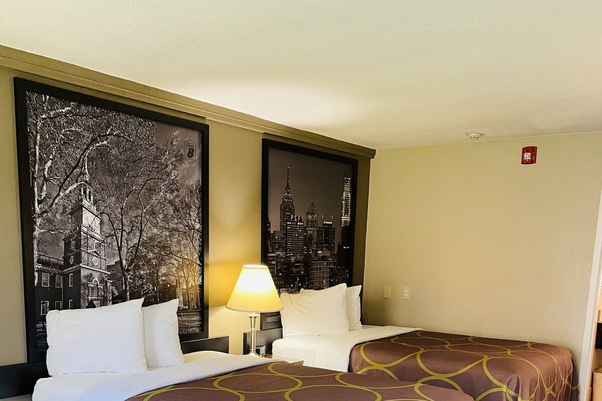 Een hotelkamer met twee bedden, een nachtkastje, een lamp en twee grote kunstwerken aan de muur met stadsgezichten.