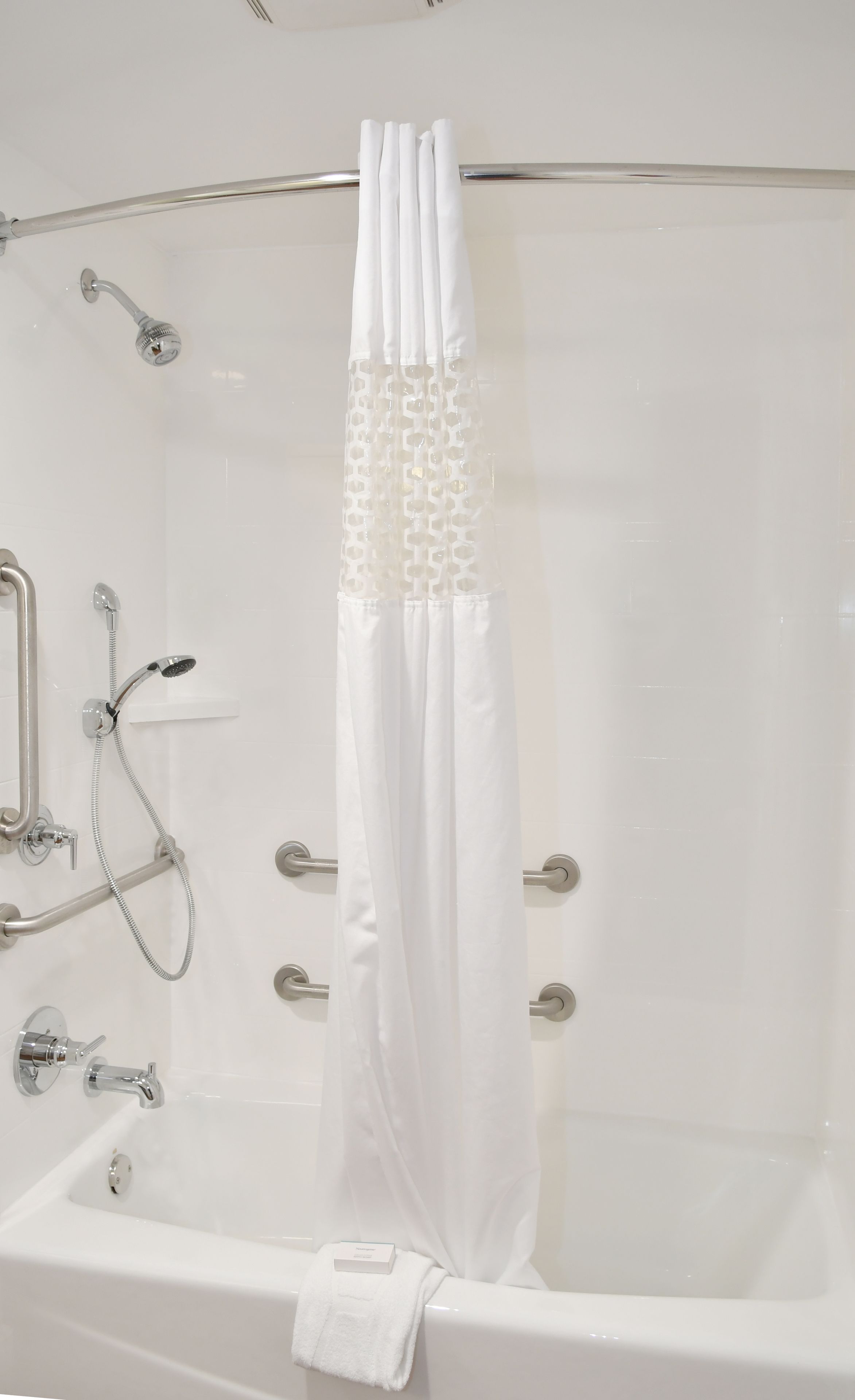 Una bañera blanca con cortina de ducha, cabezal de ducha de mano y barra de apoyo.