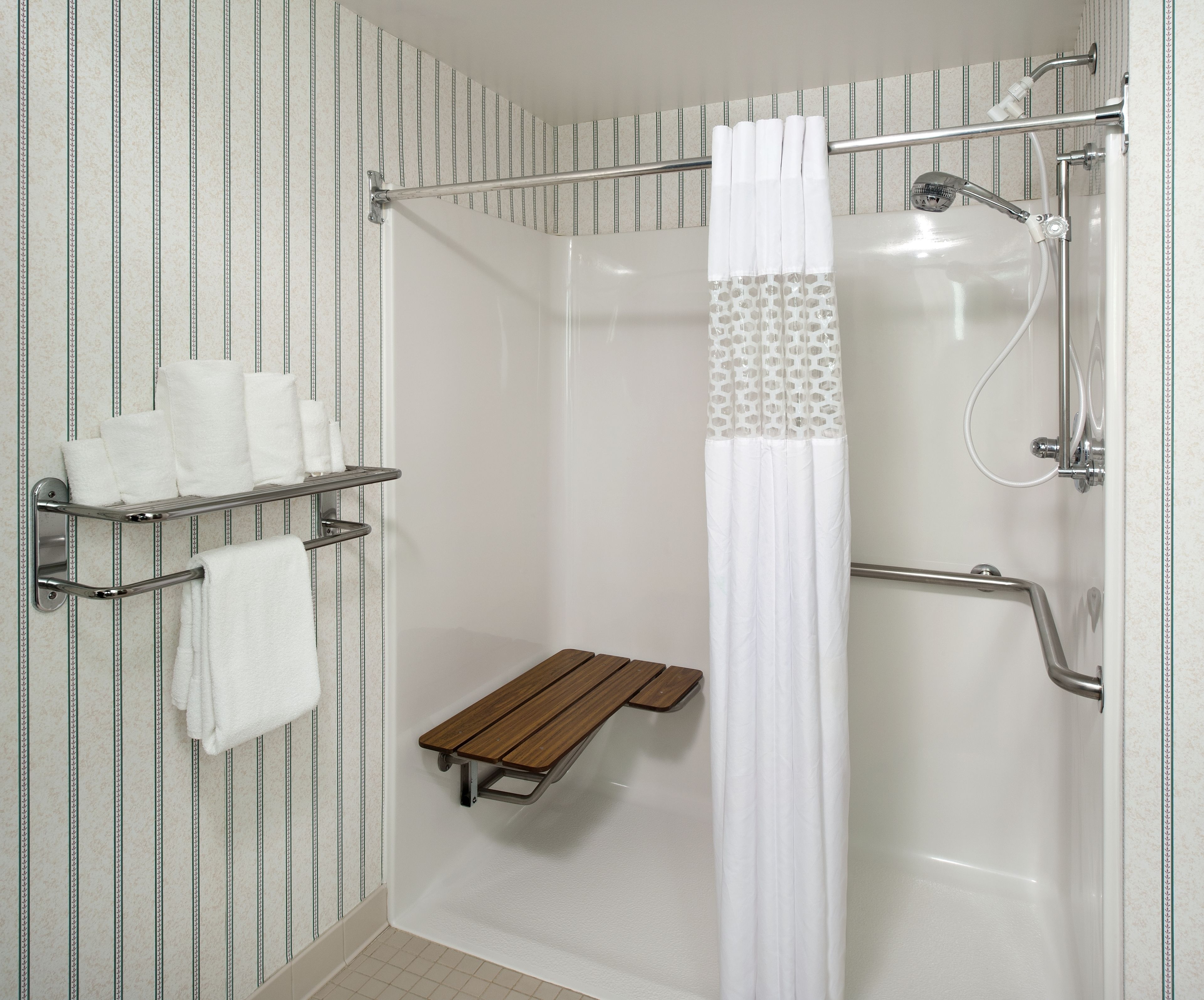 A shower with a white curtain, a wooden bench, and a towel rack with towels.