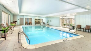 Una piscina interior con agua cristalina, rodeada de sillones de descanso y plantas en macetas.