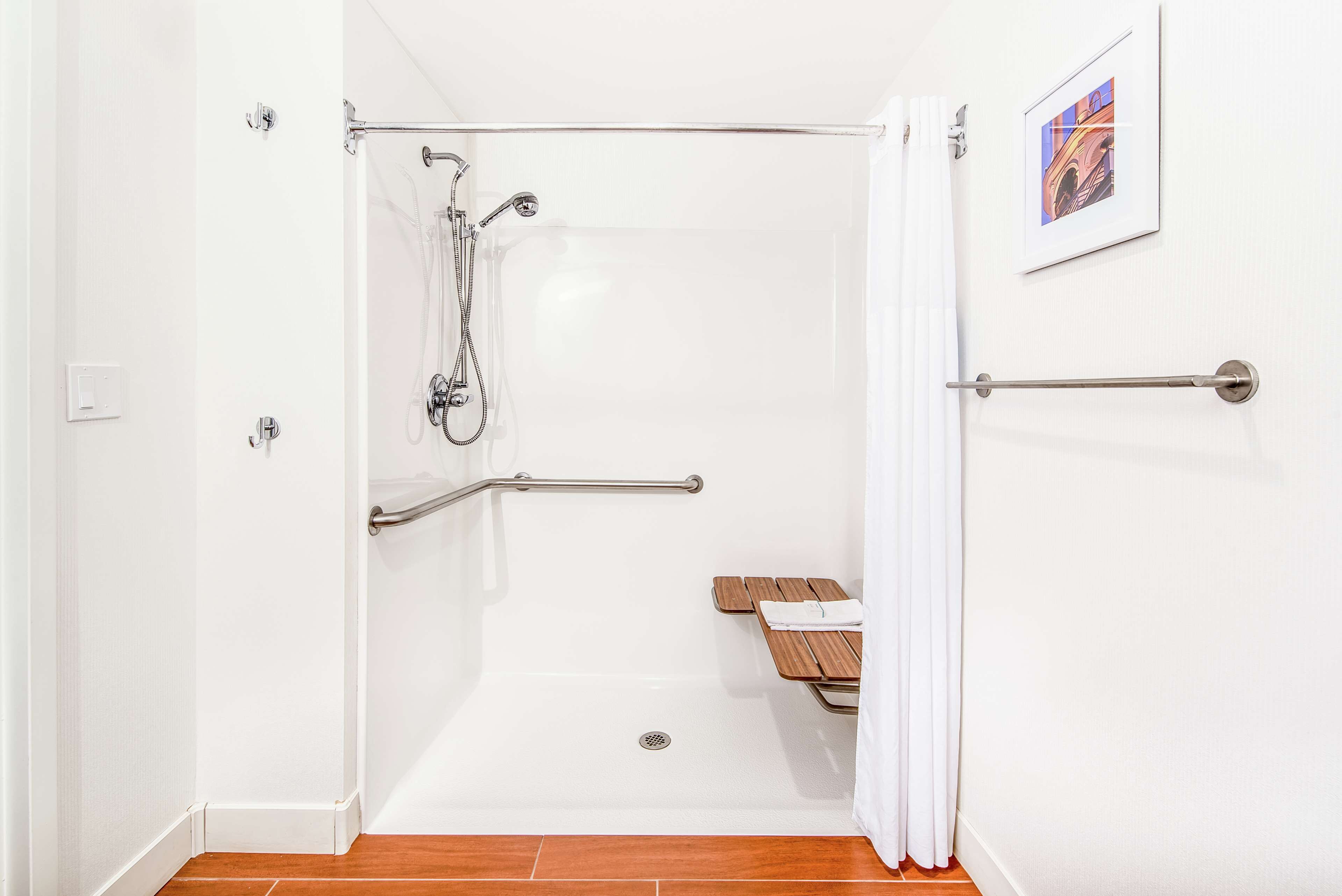 A walk-in shower with a grab bar, a wooden bench, and a framed picture on the wall.