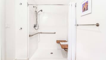 A walk-in shower with a grab bar, a wooden bench, and a framed picture on the wall.