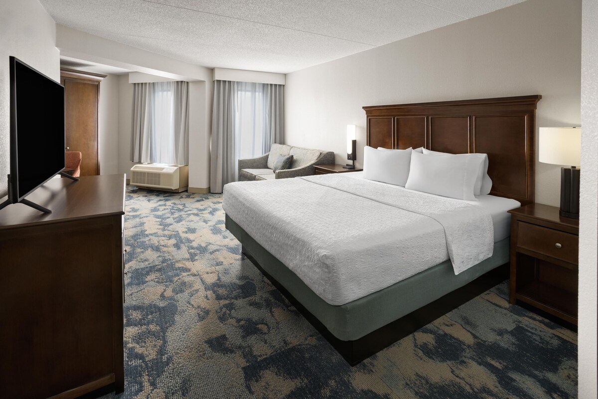 A hotel room with a large bed, a television, a desk, and a chair.
