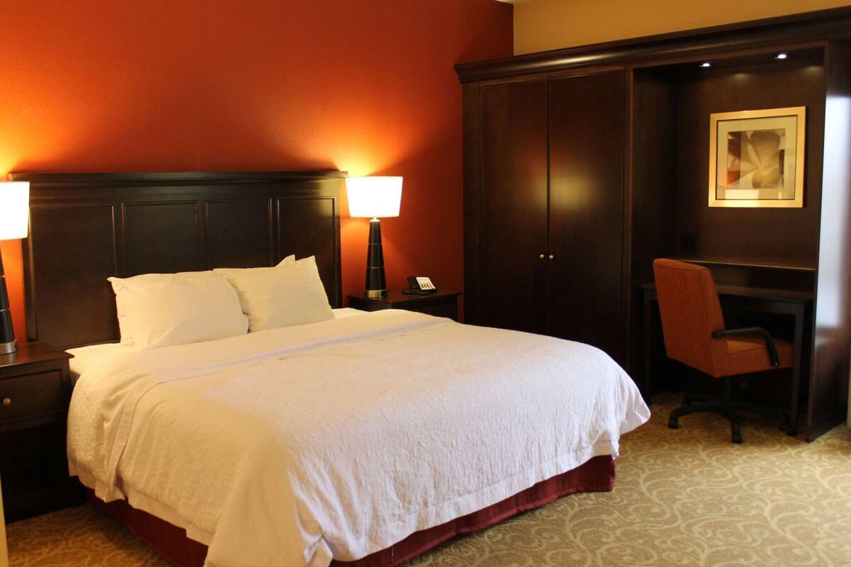 Habitación de hotel con una cama grande, dos lámparas de noche, un escritorio con una silla y un armario.