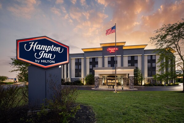 Suuri Hampton Inn by Hilton -hotelli, jossa on suuri kyltti, lippu ja moderni julkisivu.