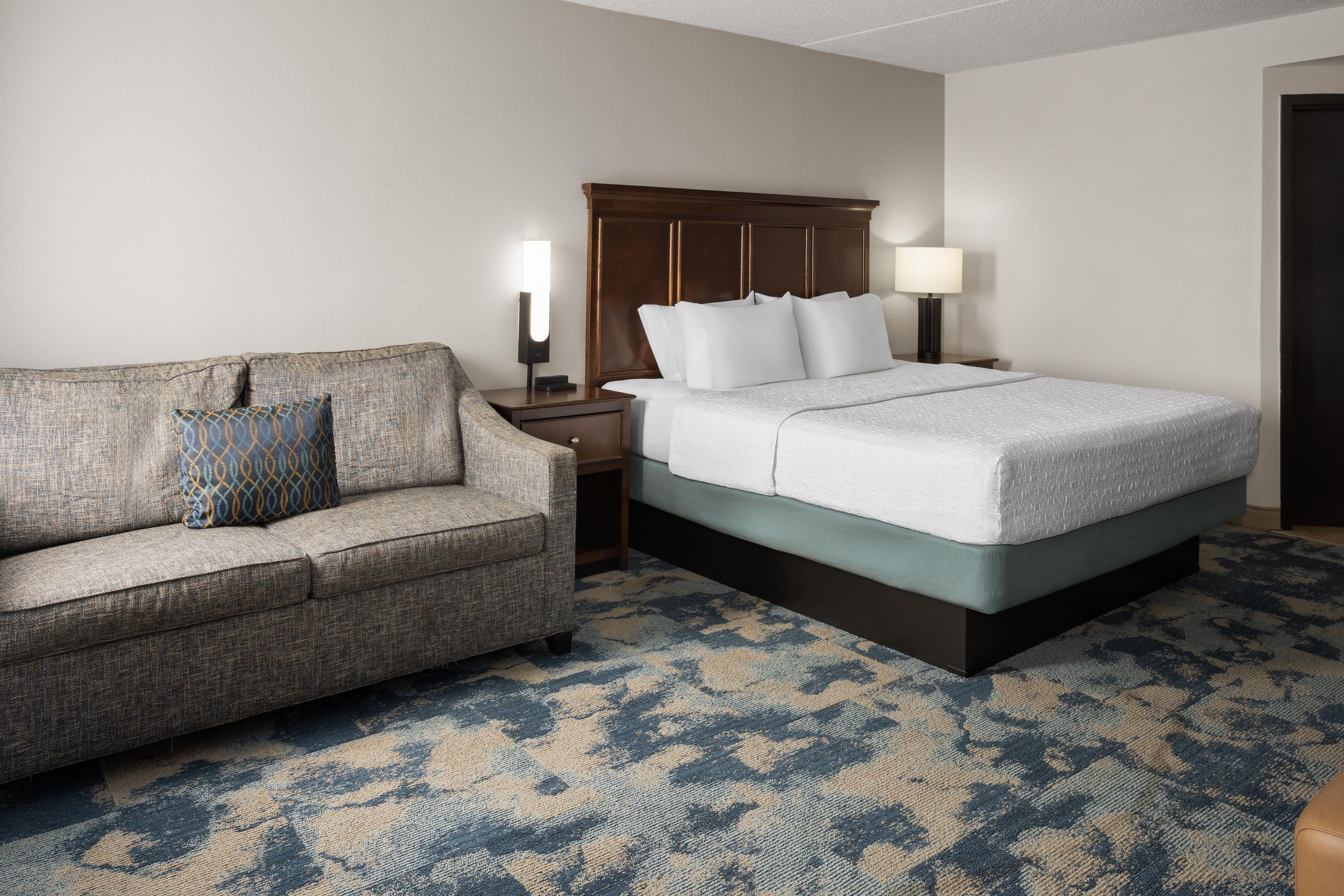 Una habitación de hotel con cama, sofá, mesita de noche y lámpara.