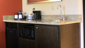 A compact hotel bathroom with a sink, a mirror, a coffee maker, and a microwave.