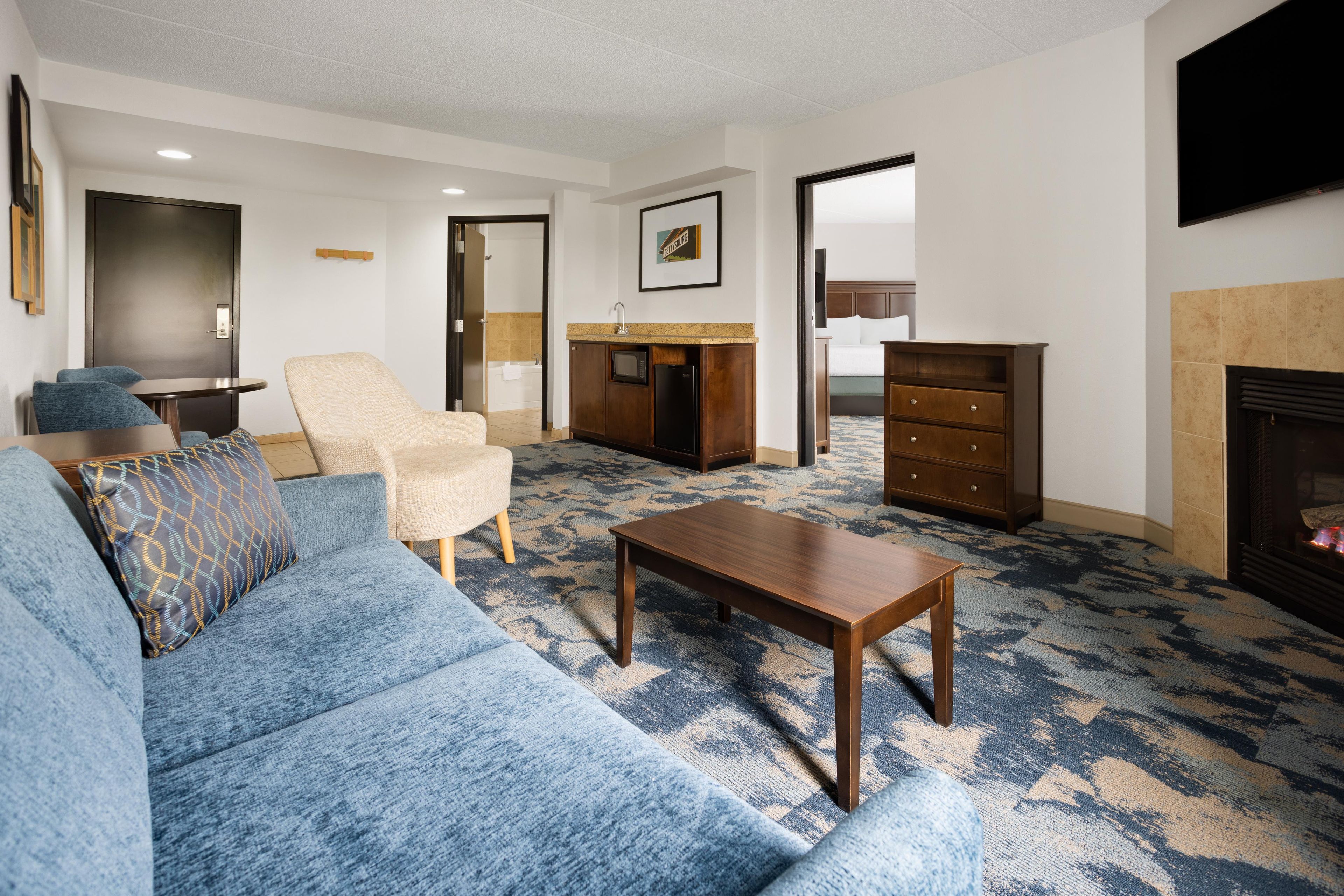 Una sala de estar con un sofá azul, una mesa de centro de madera, un sillón beige y un aparador.