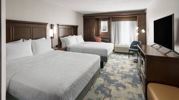 A hotel room with two beds, a desk, a television, and a window with curtains.