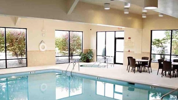 An indoor swimming pool with clear glass walls, a pool ladder, and a seating area with tables and chairs.