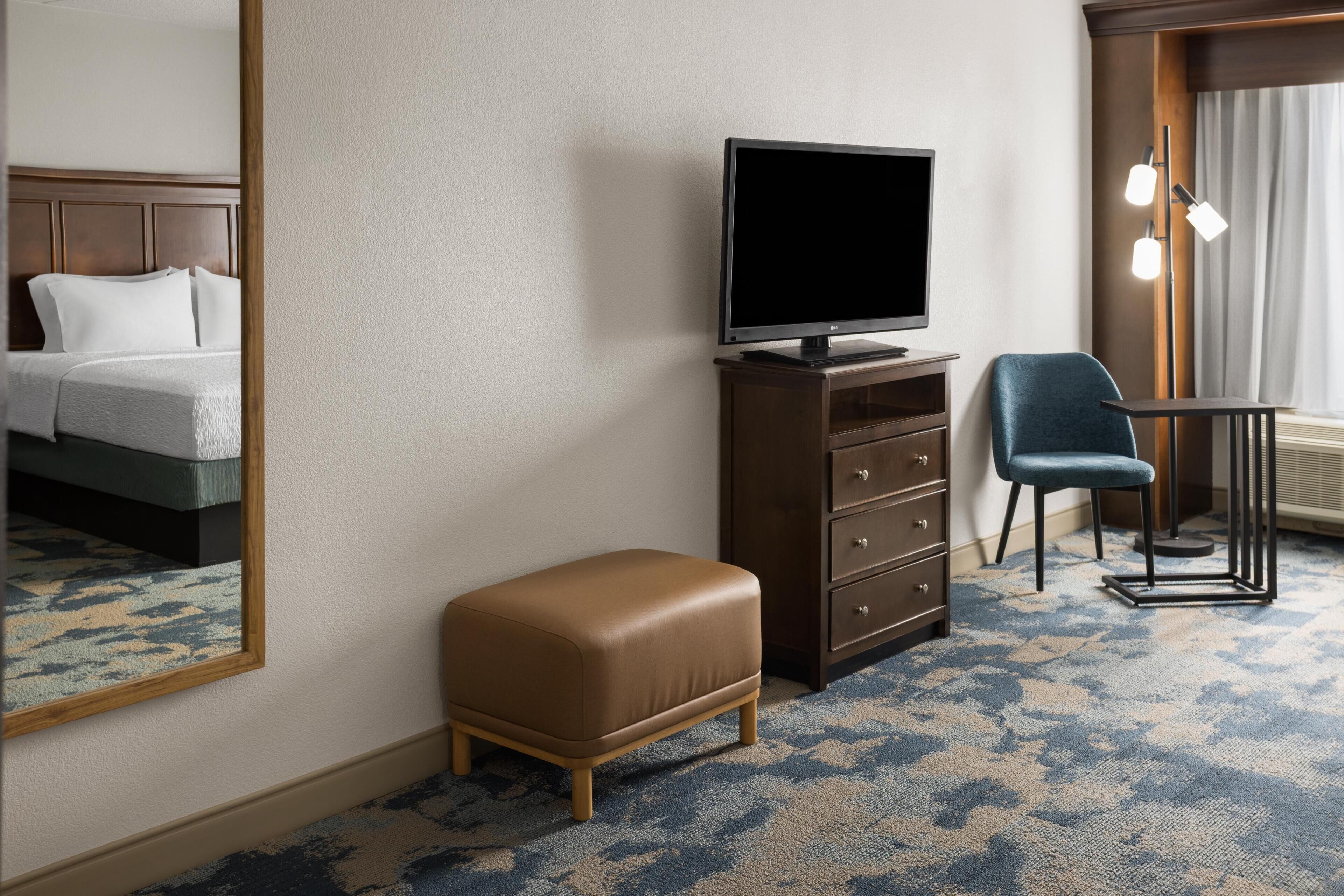 A hotel room with a bed, a television on a dresser, a chair, and a mirror.