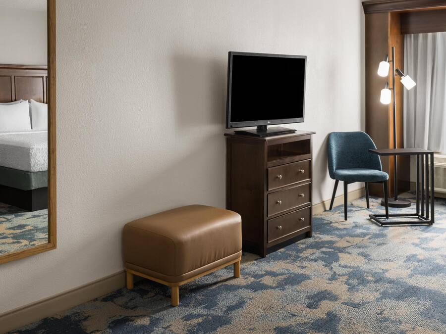 A hotel room with a bed, a television on a dresser, a chair, and a mirror.