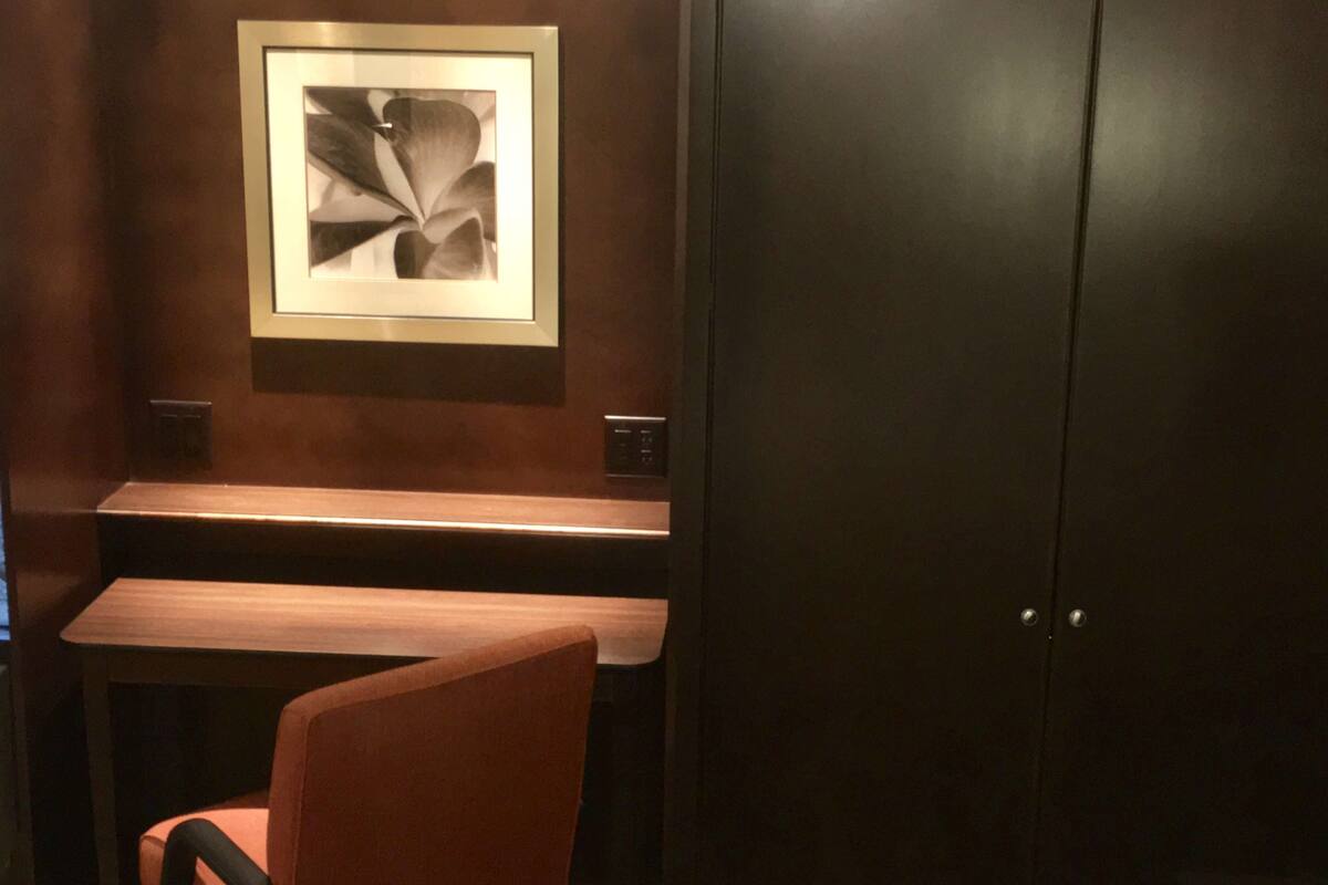 Una habitación con una puerta de madera oscura, una obra de arte abstracta enmarcada en la pared, un banco de madera y una silla naranja.