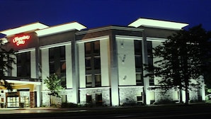 A Hampton Inn hotel with a modern design, featuring a prominent red sign, large windows, and a welcoming entrance.