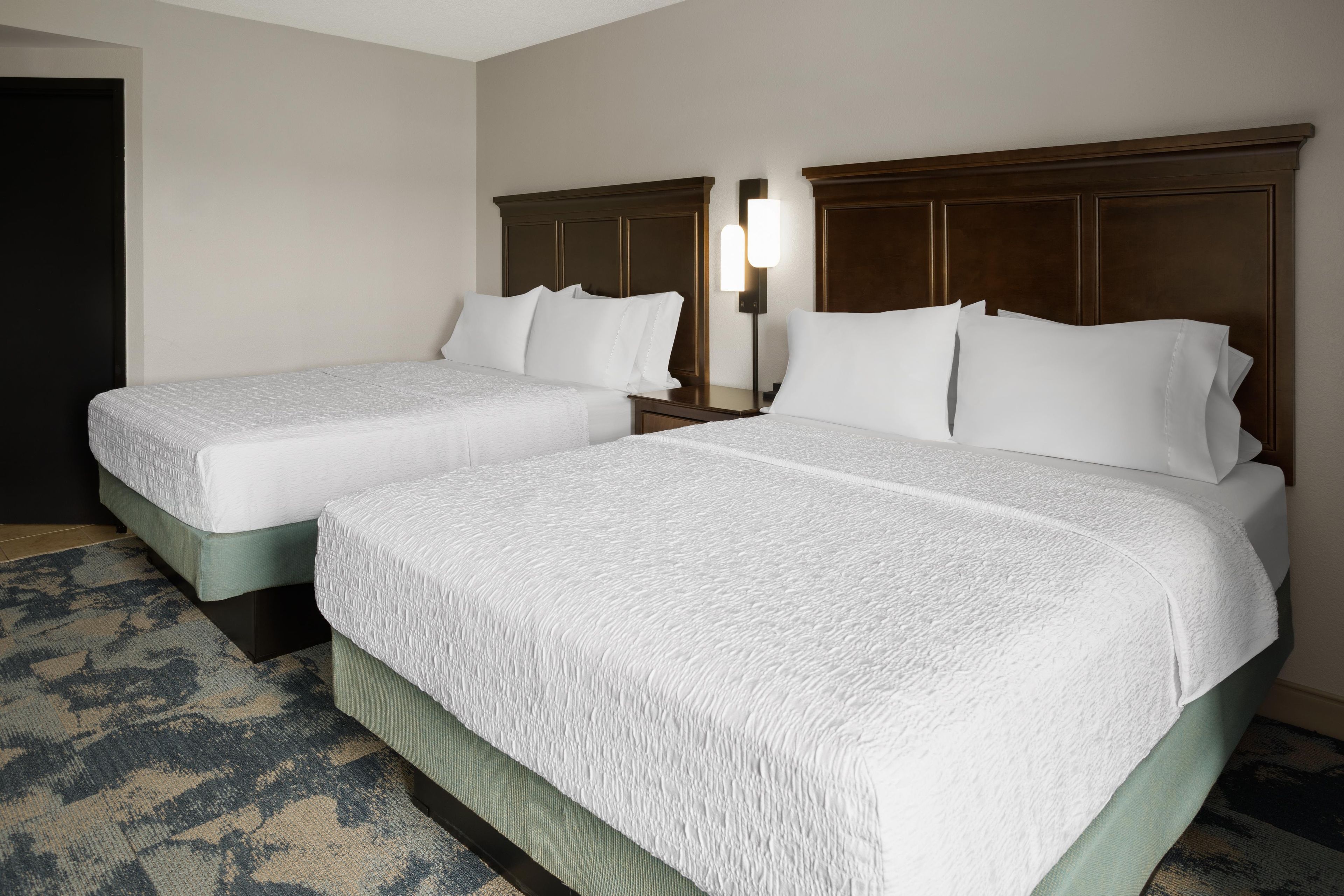 A hotel room with two beds, a nightstand, and a lamp.