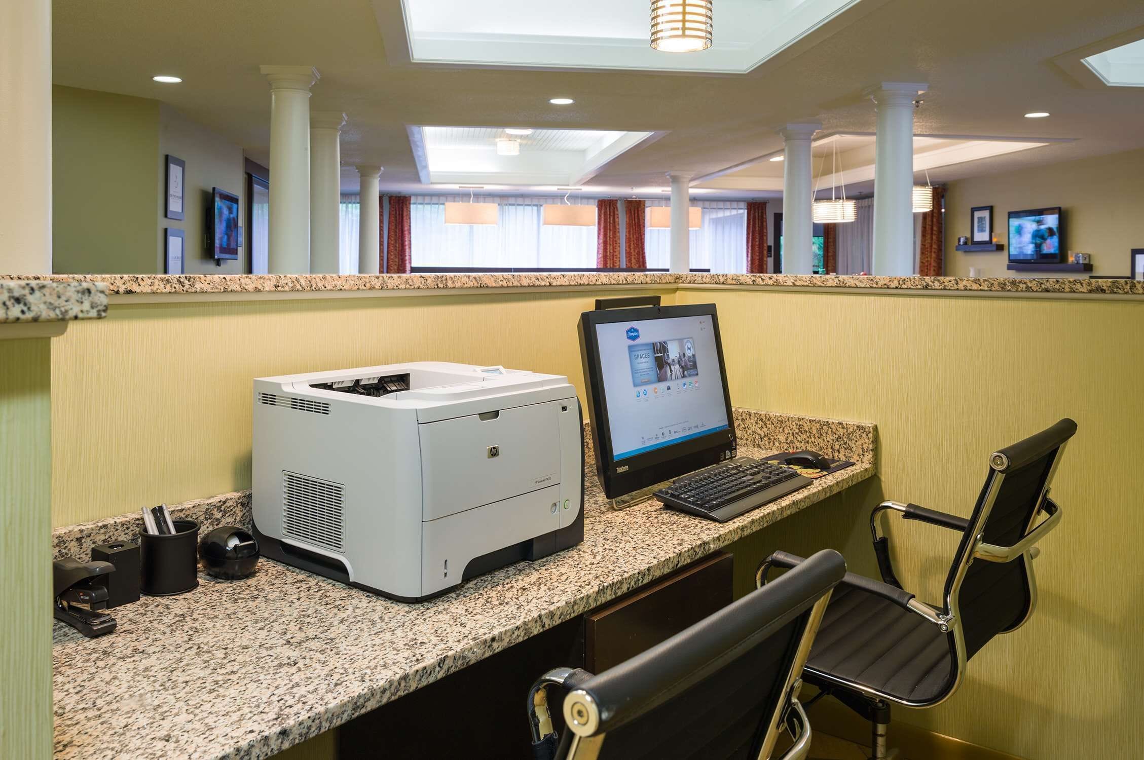Un mostrador de recepción con una computadora de escritorio, una impresora y una silla.