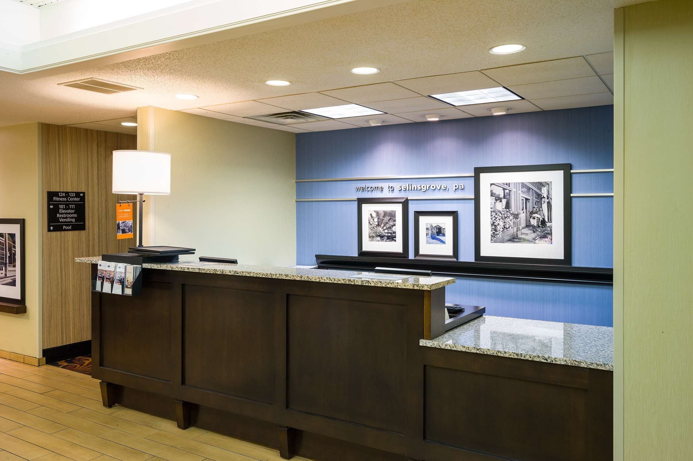 A reception desk with framed pictures, a sign indicating the fitness center, and a directory for room numbers and amenities.