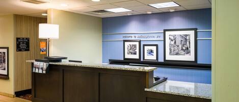 A reception desk with framed pictures, a sign indicating the fitness center, and a directory for room numbers and amenities.