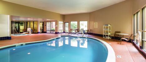 Una piscina interior con agua cristalina, rodeada de sillones de descanso y una pequeña mesa.