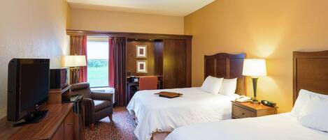 A hotel room with two beds, a desk with a television, a chair, a desk lamp, and a nightstand with a phone.