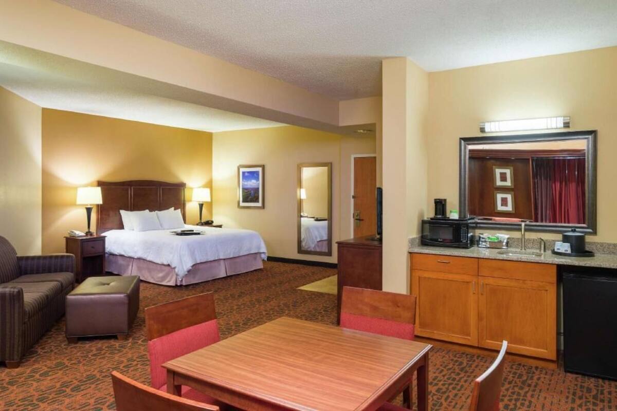 Habitación de hotel con cama, escritorio, silla, sofá, una mesita, microondas, cafetera y espejo.
