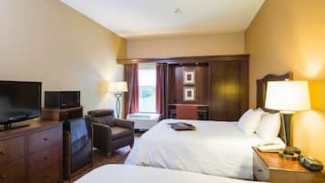 Een hotelkamer met twee bedden, een televisie, een bureau met lamp, een stoel en een bureaulamp.
