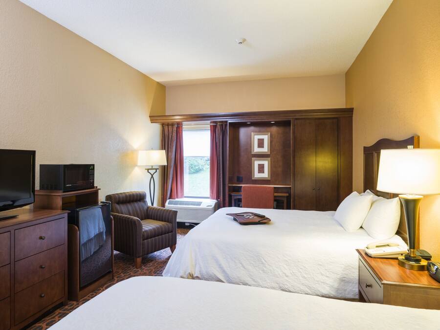 Een hotelkamer met twee bedden, een televisie, een bureau met lamp, een stoel en een bureaulamp.